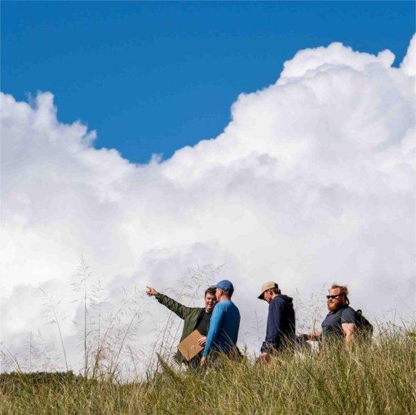 Clouds loom in the background as college students walk through tall beach grass on an outdoor classroom assignment.